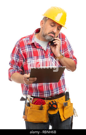 Male builder talking on the phone checking notes on clipboard with confused expression isolated on white background Stock Photo