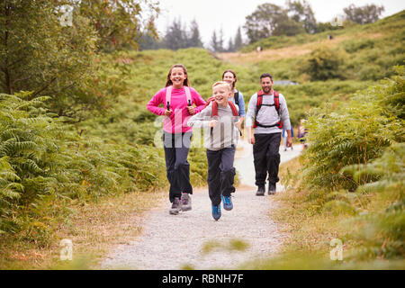 Children running ahead of parents walking on a country path during a family camping trip, selective focus Stock Photo