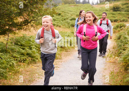 Close up of children running ahead of parents on a country path during a family vacation, front view Stock Photo