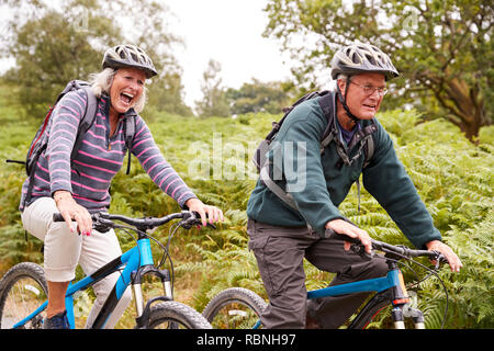 Senior couple riding mountain bikes in the countryside during a camping holiday, side view, close up Stock Photo