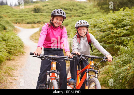 Two children sitting on their mountain bikes on a country path laughing, front view Stock Photo