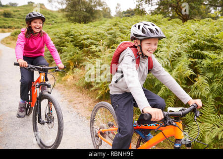 Two children riding mountain bikes on a country path laughing, selective focus Stock Photo