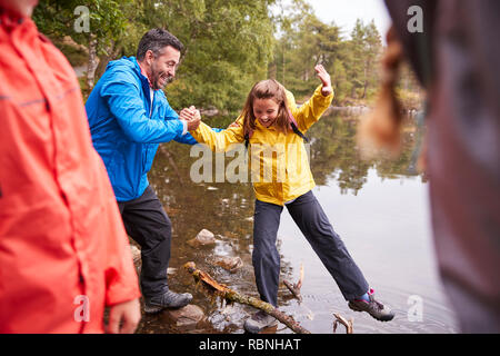 Middle aged father holding his daughter’s hand while she balances on the shore of a lake, Lake District, UK Stock Photo