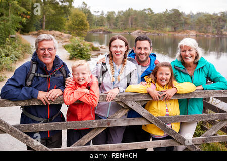 Multi generation family standing behind a wooden fence looking to camera, Lake District, UK Stock Photo