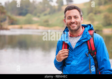 Adult man on a camping holiday standing by a lake smiling to camera, portrait, Lake District, UK Stock Photo