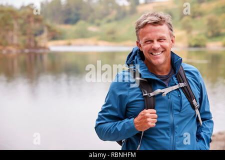 Adult man on a camping holiday standing by a lake smiling to camera, close up, Lake District, UK Stock Photo