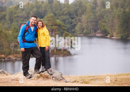 Caucasian pre-teen girl standing with her father on a rock by a lake, smiling to camera, lakeside background Stock Photo