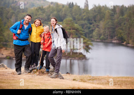 Young family standing on a rock by a lake looking to camera embracing, full length Stock Photo