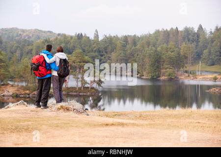 Young adult couple standing on a rock admiring the lakeside view, back view Stock Photo