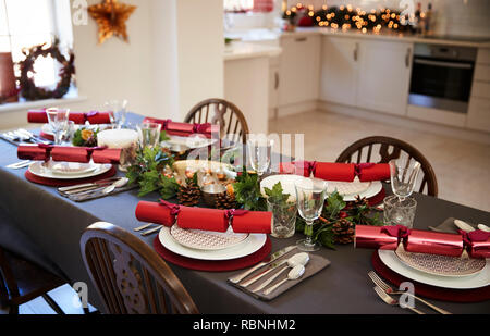 Christmas table setting with Christmas crackers arranged on plates in a dining room, with kitchen in the background Stock Photo