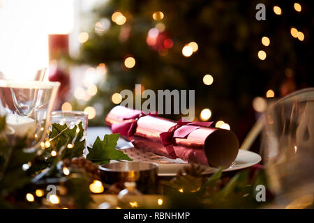Close up of Christmas table setting with a Christmas cracker arranged on a plate and Christmas tree in the background Stock Photo