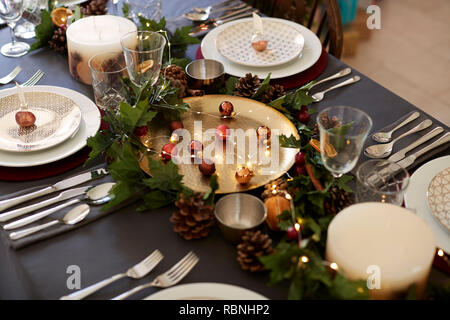 Christmas table setting with bauble name card holders arranged on plates, golden plate centrepiece with baubles, and green and red table decorations, elevated view Stock Photo