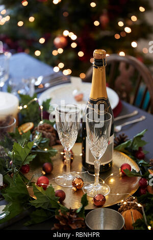 Christmas table setting with glasses and a bottle of champagne, baubles arranged on a gold plate and green and red table decorations, vertical Stock Photo