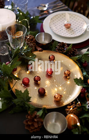 Christmas table setting with baubles on golden plate, bauble name card holder arranged on plate and green and red decorations, close up Stock Photo
