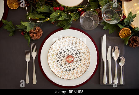 Christmas table place setting with bauble arranged on a plate and green and red table decorations, overhead view Stock Photo