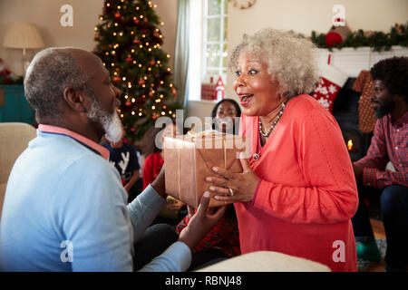 Senior Couple Exchanging Gifts As They Celebrate Christmas At Home With Family Stock Photo
