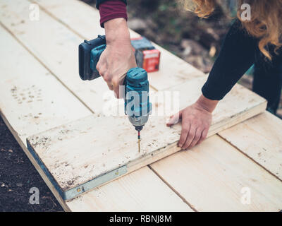 A young woman is using an impact driver outdoors in the winter Stock Photo