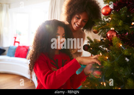 Mother And Daughter Hanging Decorations On Christmas Tree At Home Stock Photo