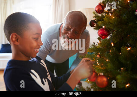 Grandfather And Grandson Hanging Decorations On Christmas Tree At Home Together Stock Photo