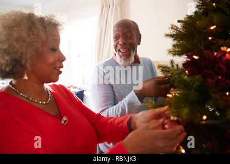 Senior Couple Hanging Decorations On Christmas Tree At Home Together Stock Photo