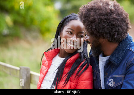 Happy black couple leaning on a fence in the countryside looking into each other’s eyes, close up Stock Photo