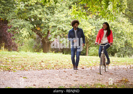 Black couple having fun in a park, the woman riding a bike, front view