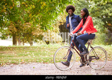 Black man running in a park beside his girlfriend, who is riding a bike, side view