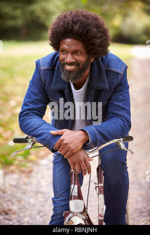 Black middle aged man sitting on a bike in  a park, leaning on the handlebars smiling, front view, close up Stock Photo