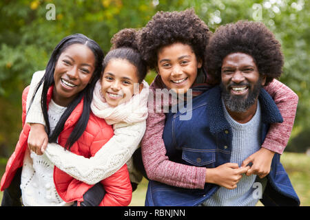 Mixed race family smiling to camera, parents piggybacking kids in the countryside, close up