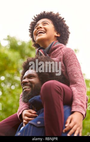 Black middle aged man carrying his son on his shoulders in the park, close up, low angle Stock Photo