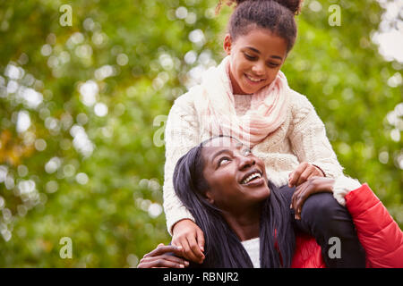 Young black woman carrying her pre-teen daughter on her shoulders in the park, both smiling at each other, close up Stock Photo