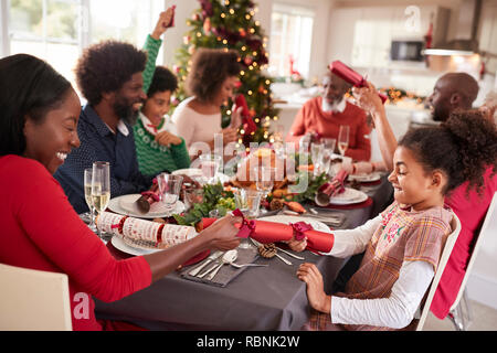 Mixed race, multi generation family having fun pulling crackers at the Christmas dinner table