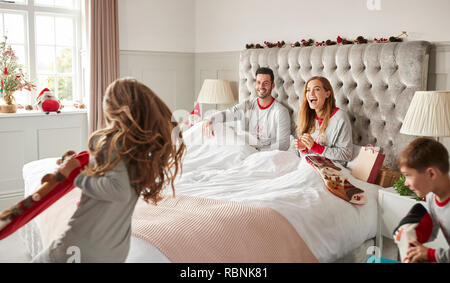 Excited Children Running Into Parents Bedroom At Home With Stockings As Family Open Gifts On Christmas Day Stock Photo