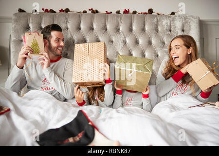 Excited Family In Bed At Home Shaking Gift Boxes On Christmas Day Stock Photo