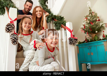 Portrait Of Excited Family Wearing Pajamas Sitting On Stairs On Christmas Morning Stock Photo