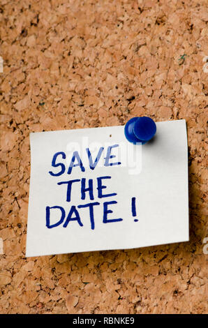 Save the date message on sticker note pin on cork office board. Reminder for registration or appontment written on card. Business concept. Stock Photo