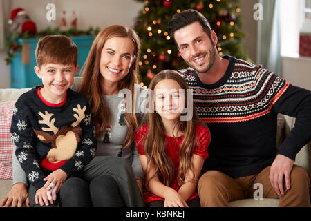 Portrait Of Parents With Children Wearing Festive Jumpers Sitting On Sofa In Lounge At Home On Christmas Day Stock Photo