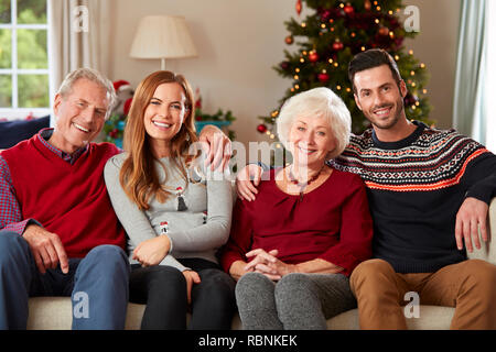 Portrait Of Senior Parents With Adult Offspring Wearing Festive Jumpers Sitting On Sofa In Lounge At Home On Christmas Day Stock Photo