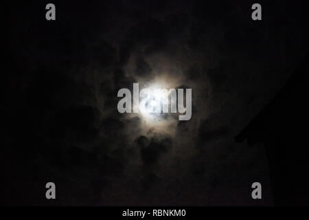 Full Moon Appearing Through Clouds At Night Stock Photo