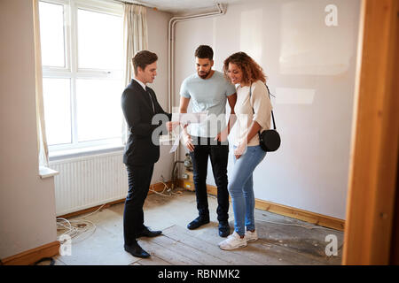 Couple Buying House For The First Time Looking At Survey With Realtor Stock Photo