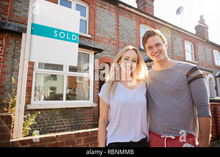Portrait Of Excited Couple Standing Outside New Home With Sold Sign ...