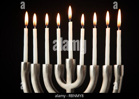 Lit Candles On Metal Hanukkah Menorah Against Black Studio Background Stock Photo
