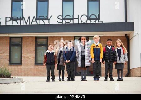 Primary school kids standing in front of their school looking to camera, full length, low angle Stock Photo
