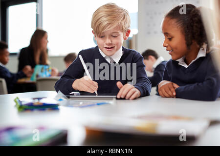 A girl and a boy using a tablet computer and stylus in a primary school class, front view, selective focus Stock Photo