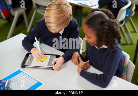 Elevated view of a girl and a boy using a tablet computer and stylus together in a primary school class Stock Photo