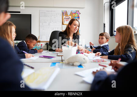 Female teacher sitting at a table with a group of schoolchildren in a primary school lesson, low angle, selective focus Stock Photo