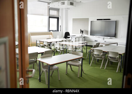 An empty classroom in a primary school with white desks and chairs, seen from doorway Stock Photo