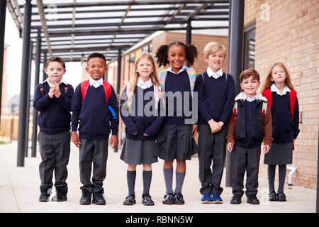 Primary school kids standing in a row on a walkway outside their school, smiling to camera, low angle Stock Photo