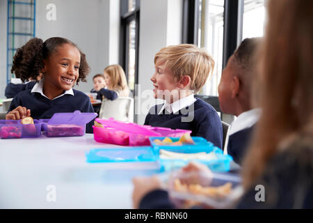 Primary school kids sitting at table eating their packed lunches and talking, close up Stock Photo