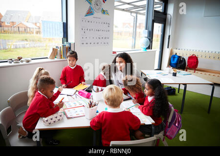 A group of infant school kids sitting at a table in a classroom with their female teacher Stock Photo